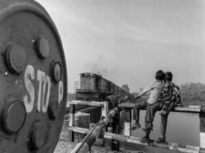 Kids love trains, whether they are inside or outside of them| Here two kids watch the passenger service to Bahraich pass the crossing at Manjhra Purab before heading off to the fields for cutting sugarcane